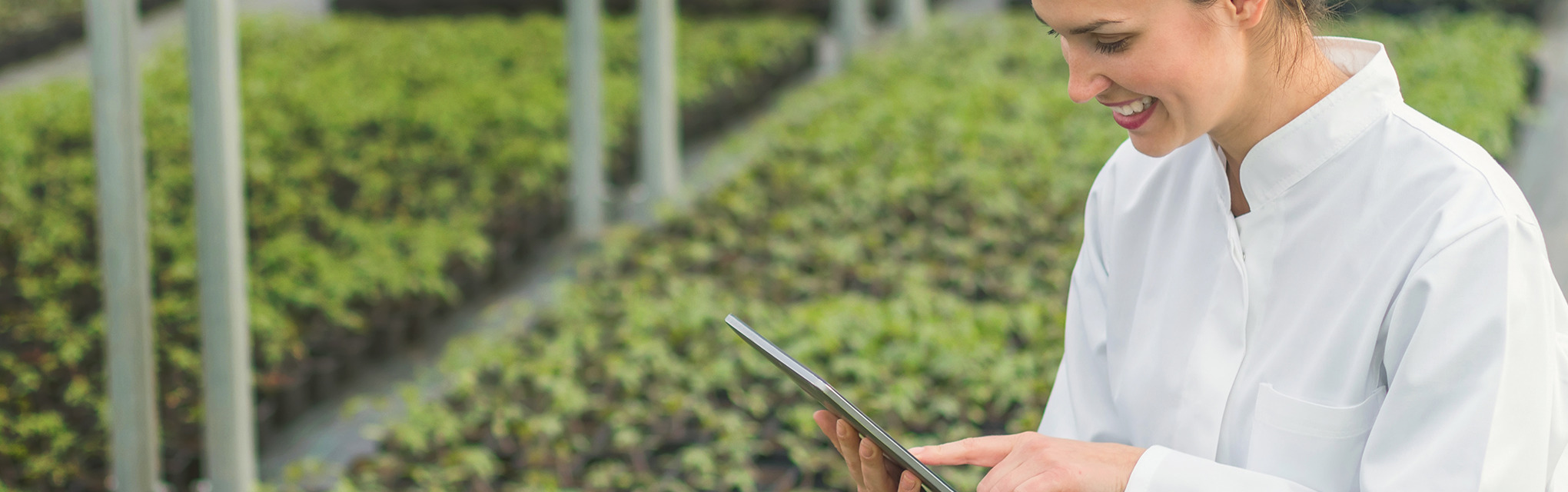 A woman in a white coat holding a tablet in a garden, representing sustainability and conscious consumerism solutions.