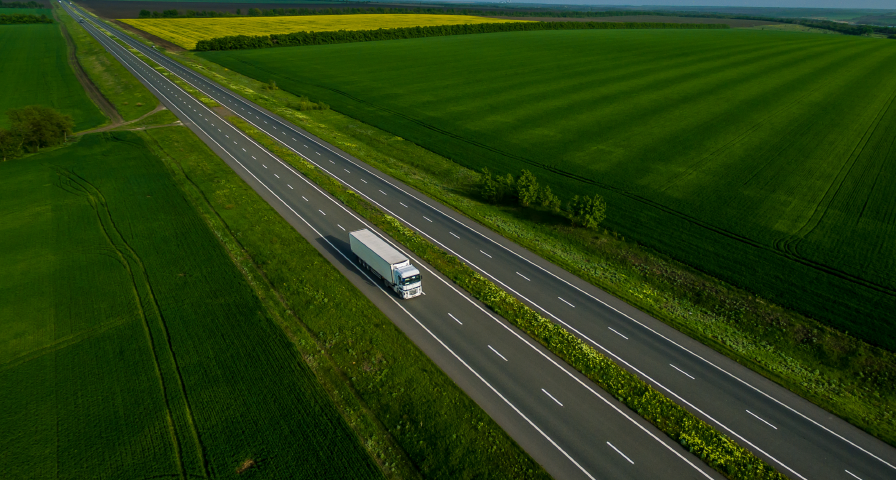 A truck traveling on a road through green fields, representing inflation and the role of digital technologies.